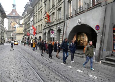 Marktgasse Bern, im Hintergrund die Zytglogge. Eine Gruppe Menschen läuft die Gasse hoch.