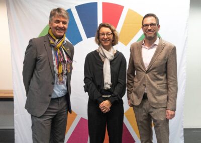 Vor grosser Leinwand mit SDG-Rad stehen Alec von Graffenried, Tatjana von Steiger und Felix Hüppi