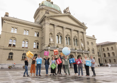 Eine Gruppe von Menschen steht mit grossen SDG-Würfeln und einer grossen Weltkugel vor dem Bundeshaus.