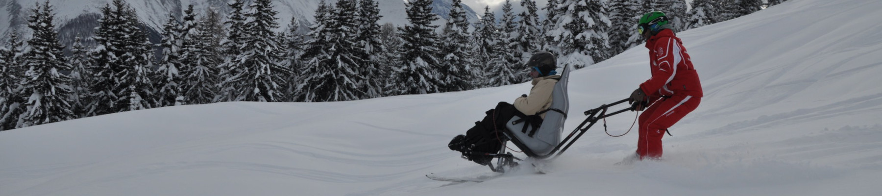 Schnee. Eine Person sitzt auf einem Ski-Sessel. Eine zweite Person steuert.