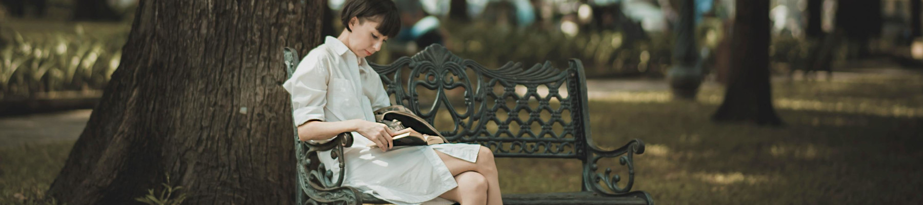 Frau sitzt auf Bank im Park. Sie liest ein Buch.